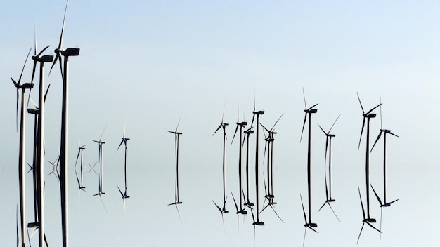 Reflection of windmills in sea against sky on sunny day