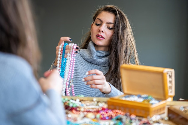 Reflection of a woman in mirror choosing and trying different jewelry soft focus closeup