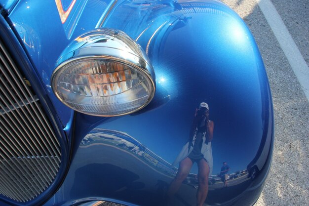 Reflection of woman photographing on old-fashioned blue car