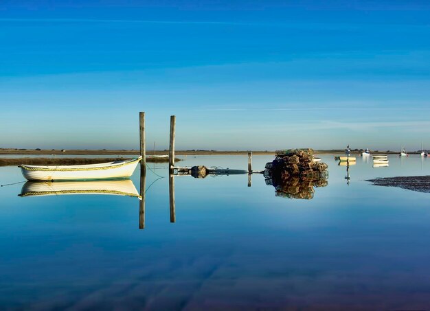 Reflection of wooden post in lake against blue sky