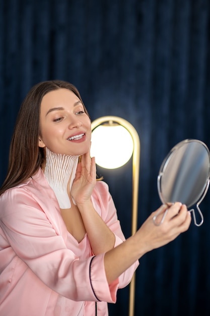 Reflection. Young woman in pink lingerie and with tapes on her neck looking in the mirror and smiling