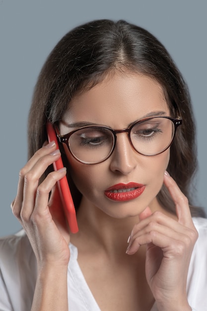 Reflections, communication. Pensive serious young woman in glasses with smartphone near ear attentive meditating