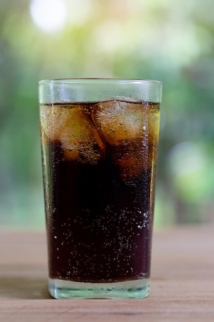 Foto bevande analcoliche rinfrescanti di soda nera o cola con ghiaccio in un bicchiere alto trasparente con sfondo naturale