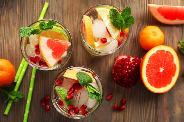 Refreshing cocktails with ice mint pomegranate seeds and slices of fruits on wooden background