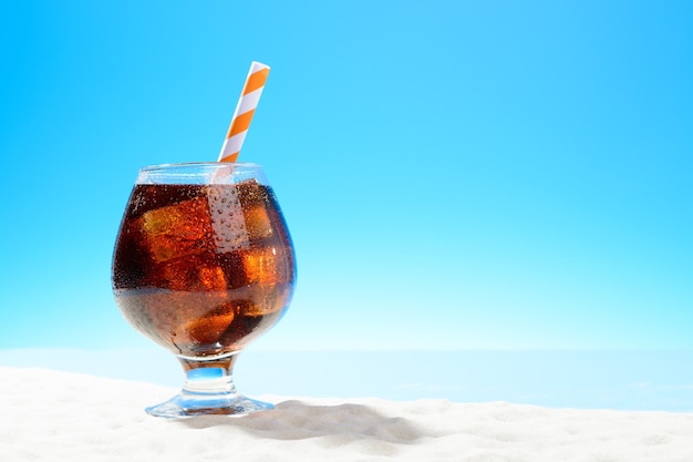 Refreshing cola with ice in glass on the sandy coast backgroundbackground