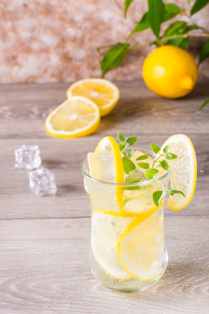 Refreshing cold mineral water with lemon, mint and ice cubes in glasses on a wooden table