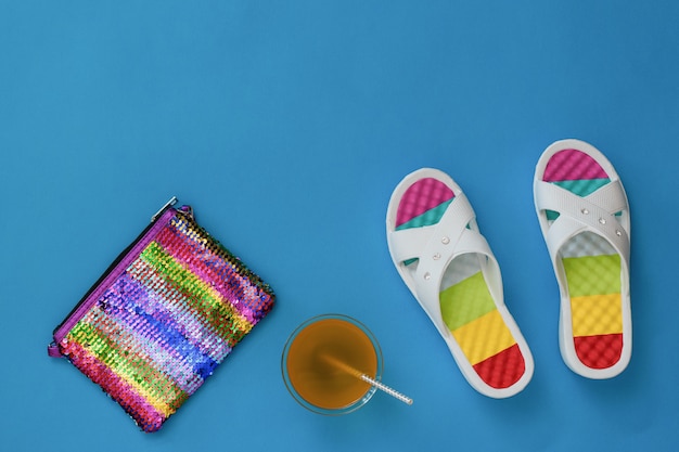 Refreshing drink, bag and flip flops on a blue surface