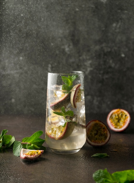 Refreshing drink with passion fruit cocktail with tropical fruit on a dark surface with green mint leaves vertical position