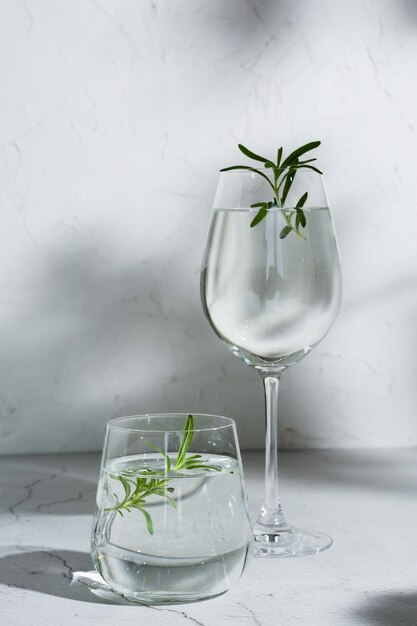 Refreshing drink with rosemary in glasses on the table in the shade of tree leaves Vertical view