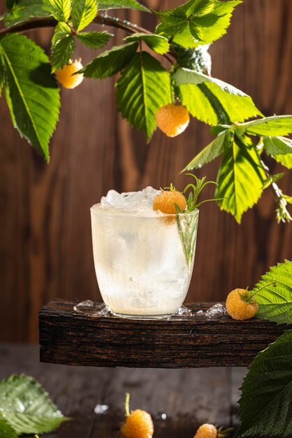 Refreshing drink of yellow raspberry surrounded raw ripe berries and green leaves Dark wooden background Backlight Ready for drinking
