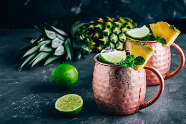 Refreshing Iced Cold Moscow Mule cocktail with lime and pineapple on dark background