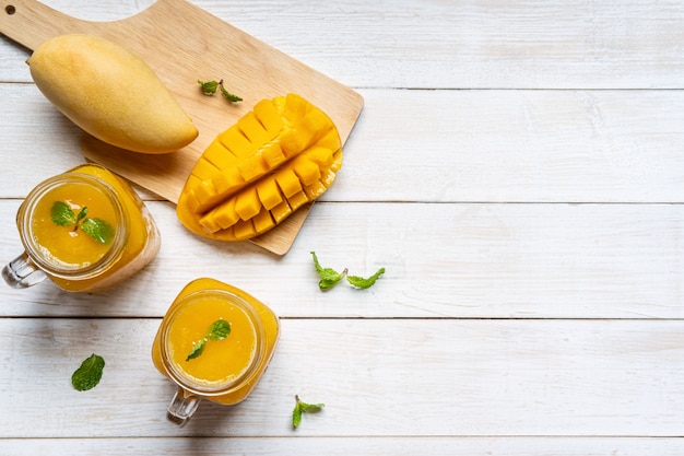 Refreshing mango smoothies in glass with ripe mango on white wooden table and copyspace, Top view