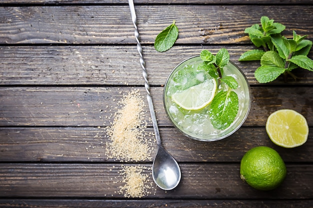 Refreshing mint cocktail mojito with rum and lime, cold drink or beverage with ice on white wooden surface, top view