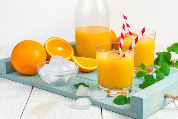 Refreshing orange juice with mint and ice cubes on a light blue board on a light desk.