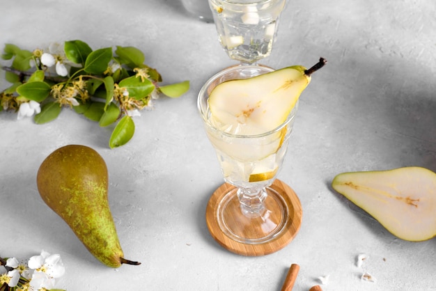 Refreshing Pear cocktail lemonade in a glasse with pear puree and fresh fruit and flowers on light gray table background