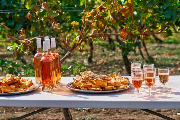 Refreshing pink wine in a glass, with pastries on a table, against the background of a vineyard