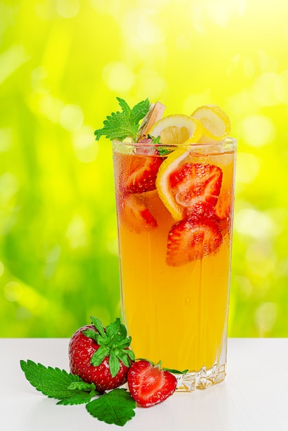 Refreshing punch with strawberries, lemon and mint on blurred sunny background.