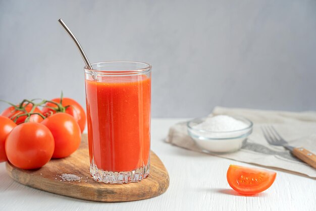 Refreshing salty tomato juice served in drinking glass with metal straw on wooden board with salt