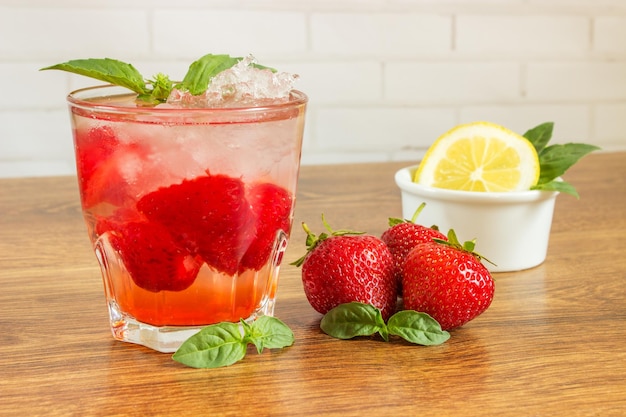 Photo a refreshing summer drink with ice strawberries and lemon on a wooden background