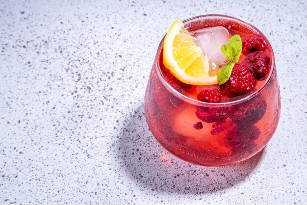 Refreshing summer infused fruit water Iced lemonade with raspberry ice cubes and mint Red berry healthy mocktail or cocktail on white background with bar utensils copy space