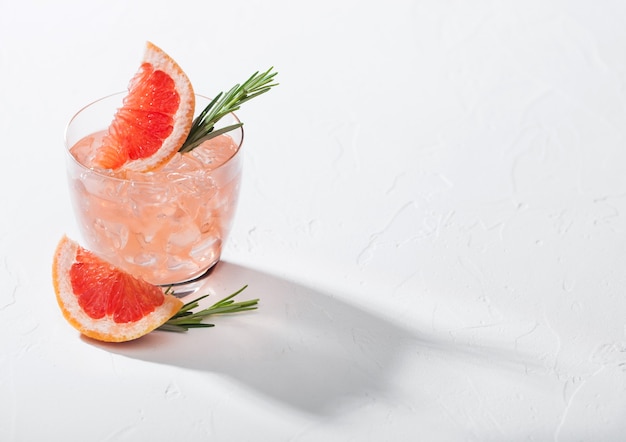 Refreshing summer red grapefruit cocktail in crystal glass with ice on white background