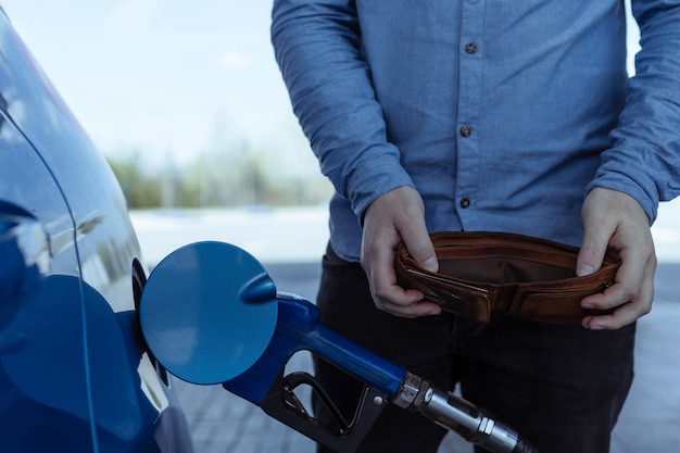 Refueling a car with gasoline at a gas station Rise in fuel prices Crisis and lack of gasoline A man holds an empty wallet near the car