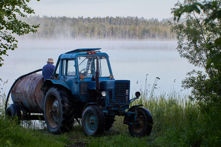 Photo refueling tractor tank with water from forest lake in early morning with fog