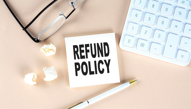 REFUND POLICY text on sticky with pen calculator and glasses on a beige background