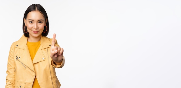 Regel nummer één Zelfverzekerde glimlachende Aziatische vrouw die wijsvinger laat zien, verbiedt het gebaar om iets af te keuren dat op een witte achtergrond staat