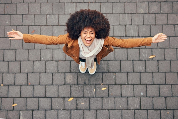 Foto regen blij en vrouw in de stad tijdens de winter buiten in de stad staan met glimlach en vreugde geluk vrijheid en opgewonden meisje uit mexico met een afro genietend van de druppels water buiten in stedelijk gebied