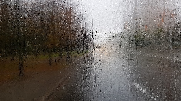 Regen op de achterruit van een auto in de herfst. Binnenaanzicht van de weg met rijdende auto's in de stad door het raam van de auto met regendruppels. het besturen van een auto in het gezichtsveld van de achterruit.