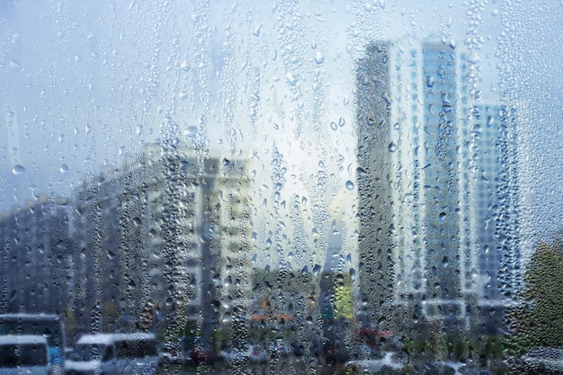 Regenachtige raamregendruppels op het glas tegen de achtergrond van een stadsstraat met huizen en een weg Zachte wazige achtergrond