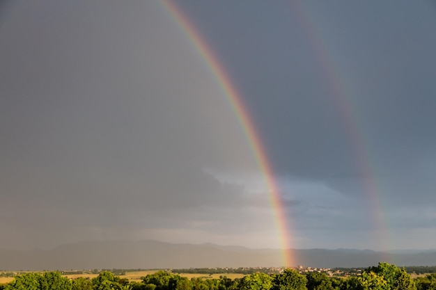 Regenboog over een schilderachtig dorp en weilanden na de regen kopiëren ruimtebehang