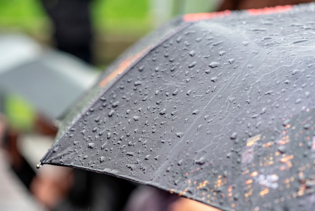Regendag, zware regen in de stad, druppels op oppervlak van zwarte paraplu, mensen met paraplu's tijdens storm