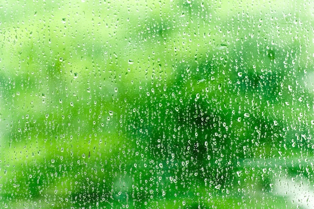 Regendalingen op de oppervlakte van vensterglazen met groene achtergrond