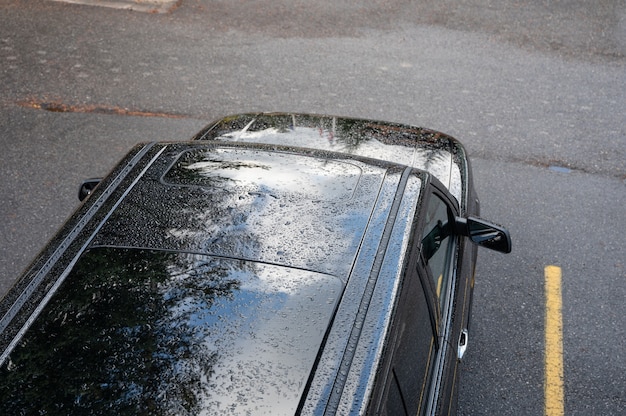 Regendruppels vallen op het dak van zwarte SUV-auto op parkeerplaats