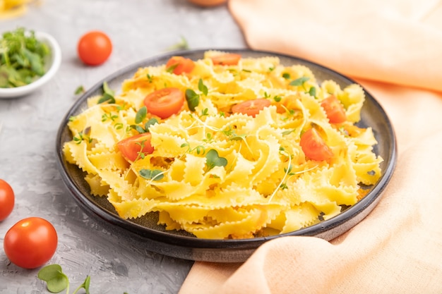 Reginelle semolina pasta with tomato, eggs and microgreen sprouts on gray