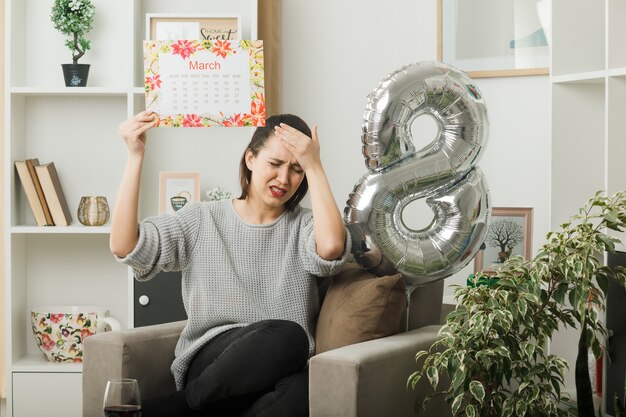 행복한 여성의 날 이마에 손을 얹은 것을 유감스럽게 생각하며 거실의 안락의자에 앉아 있는 달력을 들고 있다