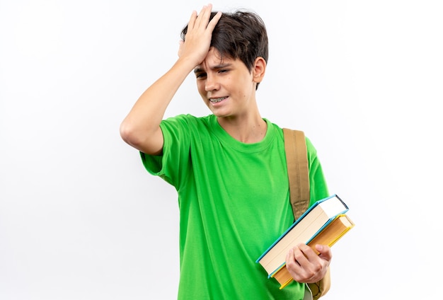 Foto deplorato giovane ragazzo della scuola che indossa uno zaino che tiene libri mettendo la mano sulla testa