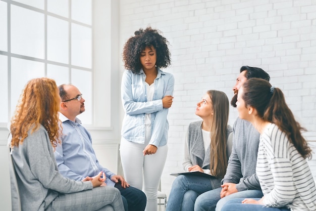 Photo rehab group listening to stressed woman standing up