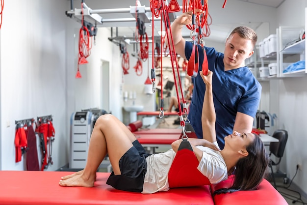 Rehabilitation specialist doing active treatment on suspension straps to female patient