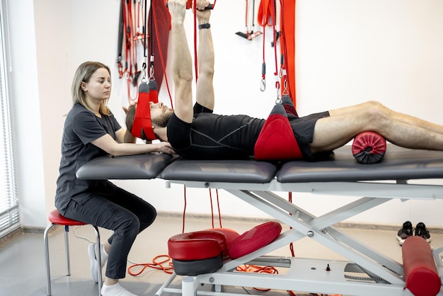 Rehabilitation specialist doing active treatment on suspension straps to a male patient