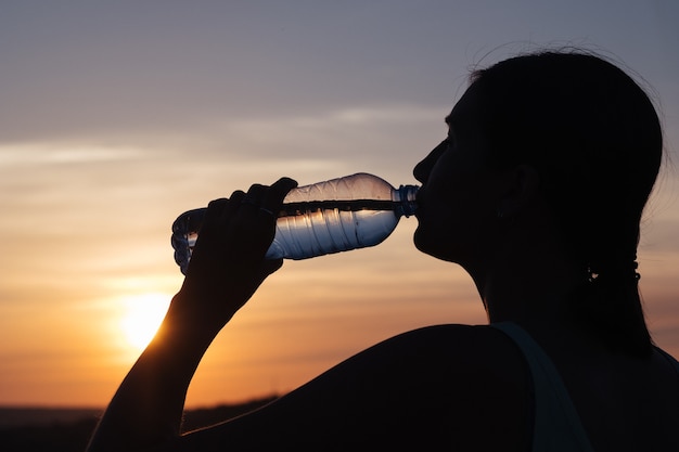 体に水分を補給します。晴れた日に屋外で水を飲むスポーティな女性。