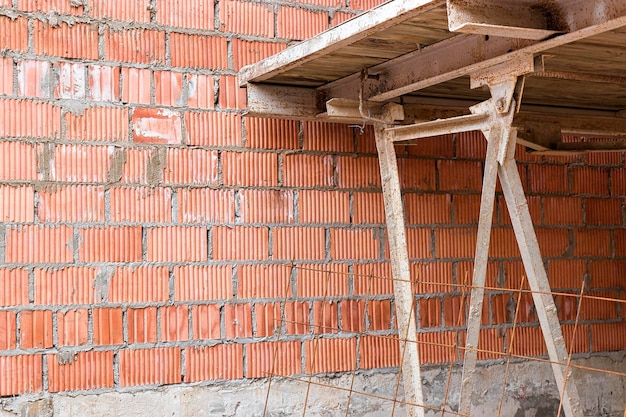 Reinforced scaffolding for the work of masons in the construction of brick walls Apparel for work on the construction site and storage of materials Closeup Construction of brick walls