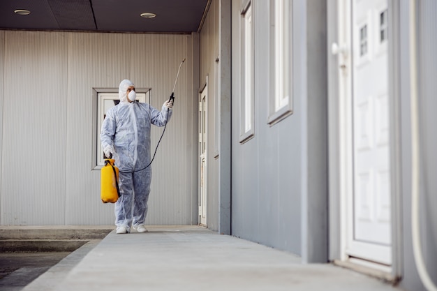 Reiniging en desinfectie buiten rond gebouwen, de coronavirus-epidemie. Professionele teams voor desinfectie-inspanningen. Infectiepreventie en bestrijding van epidemieën. Beschermend pak en masker.