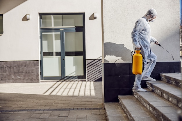 Reiniging en desinfectie buiten rond gebouwen, de covid-19-epidemie. sessieteams voor desinfectie-inspanningen. Infectiepreventie en bestrijding van epidemieën. Het pak en masker.