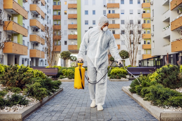 Reiniging en desinfectie buiten rond gebouwen, de covid-19-epidemie. sessieteams voor desinfectie-inspanningen. Infectiepreventie en bestrijding van epidemieën. Het pak en masker.