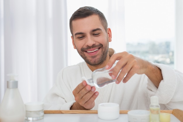 Reiniging van de huid. Positieve aardige man met behulp van een huidlotion tijdens het reinigen van zijn huid