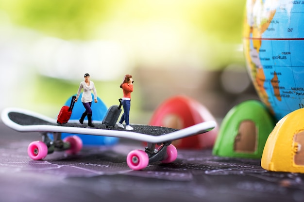 Reis de wereld rond en het avontuur. Miniatuur mensen met bagage lopen op skateboard met globe en tent bed.