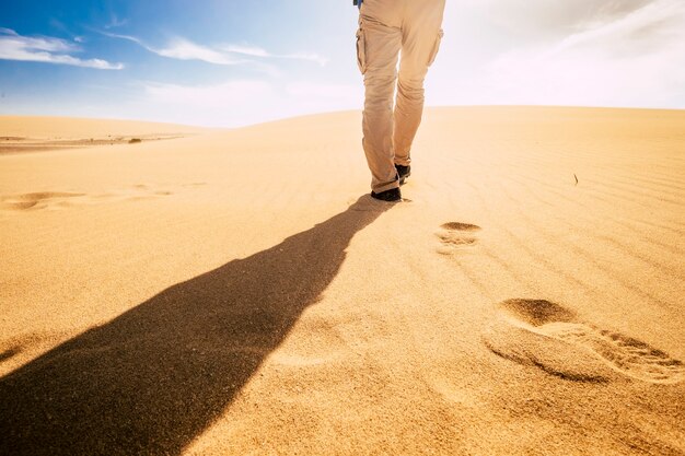 Reis en verken mensenconcept met de mens die van achteren wordt bekeken die in het zand van de woestijnduinen alleen onder de zonsondergang loopt